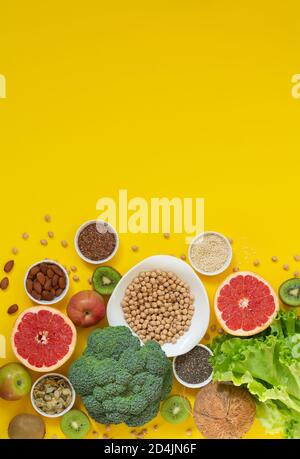 Cibo sano e una selezione di cibo pulito (verdure, frutta, semi, noci, erbe) su sfondo giallo con spazio di copia Foto Stock