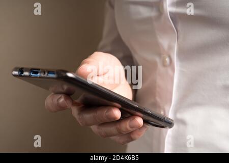 Una donna in una camicia bianca tiene un telefono su uno sfondo beige. Foto Stock