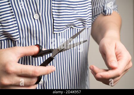 Una donna in una camicia bianca e blu sta tenendo un paio di forbici. Foto Stock