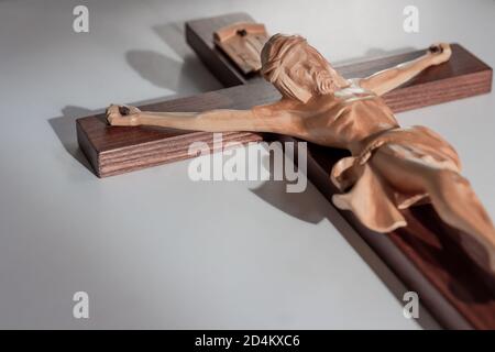 Croce crocifisso di legno cattolico su fondo bianco chiaro in caldo leggero Foto Stock
