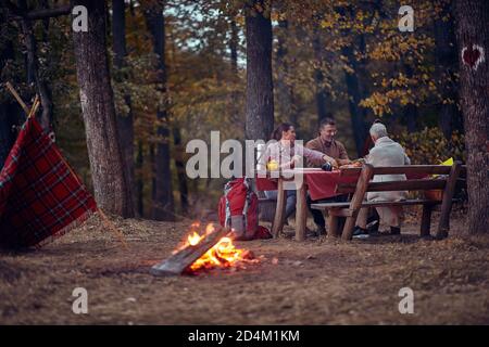 Una coppia anziana e la loro figlia hanno un picnic dentro la foresta intorno ad un falò su un bellissimo tramonto d'autunno Foto Stock