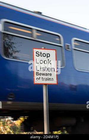 Attenzione ai treni. Sosta, guarda, ascolta le indicazioni di avvertimento all'incrocio ferroviario con il treno Greater Anglia che passa Hawkwell, Rochford, vicino a Southend, Essex, Regno Unito Foto Stock