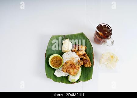 Nasi Uduk Ayam Goreng con Ice Tea, fatta in casa di famosa cucina Indonesiana. Pollo fritto con riso al vapore, verdure e tè al ghiaccio Foto Stock