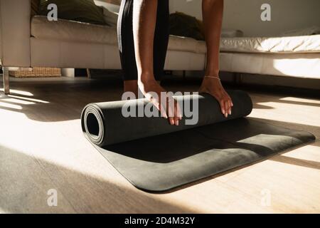 Atleta femmina che rotola fuori il tappetino di esercitazione per iniziare la sequenza di yoga in salotto. Foto Stock