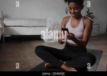 Smartphone per la navigazione di giovani donne multietniche mentre ci si allena a casa Foto Stock