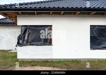 Uno strato di intonaco di silicone bianco appena applicato sulla parete della casa, la finestra angolare è protetta da un foglio nero. Foto Stock