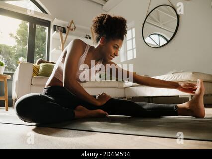 Bella donna sorridente che si allunga dopo un lungo flusso di yoga seduta sopra tappetino yoga nella moderna sala Foto Stock