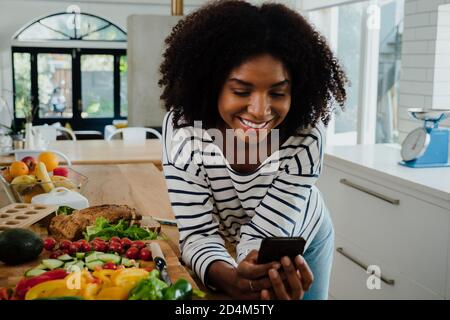 Bella donna con afro in cucina navigazione dispositivo mobile Foto Stock