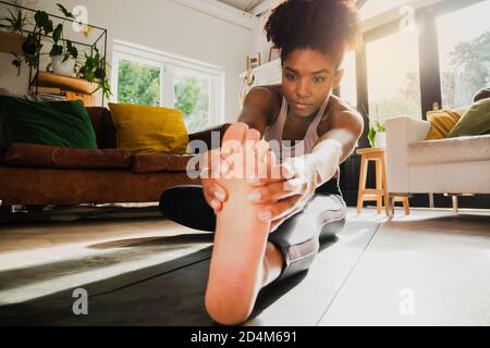 Giovane donna che lavora fuori da casa e allunga le gambe su tappetino yoga Foto Stock