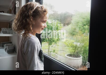 Piccola ragazza caucasica che guarda fuori la pioggia su un mattina invernale tempestosa Foto Stock