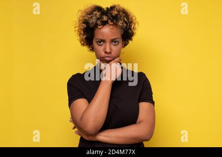 Giovane donna afroamericana che pensa, tenendo la mano sul mento che fa un piano Foto Stock
