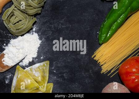 Vista dall'alto sullo sfondo della pasta con spaghetti, ravioli, pepe verde, cipolla e patate su sfondo scuro floury.Healthy cucina casalinga concept.Copy sp Foto Stock