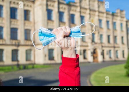 La quarantena è troppo concettualmente. Foto ravvicinata della mano che si alza la maschera medica di fronte all'edificio universitario Foto Stock