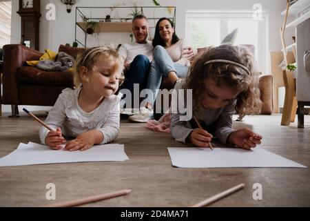 Famiglia caucasica nella sala insieme trascorrere del tempo di qualità, figlia disegnare le immagini sul pavimento come i genitori guardare sopra Foto Stock