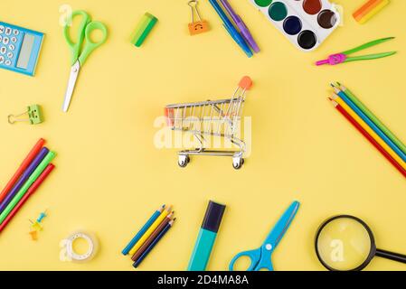 Concetto di shopping di ritorno alla scuola. In alto vista dall'alto foto di piccolo carrello e colorata cancelleria isolata su sfondo giallo Foto Stock