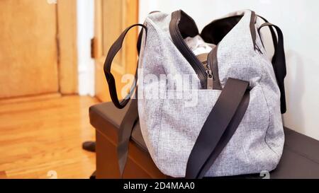 borsa da palestra in borsone grigio per lo sport e il fitness, una borsa aperta senza marchio piena di vestiti sul tavolo con sfondo della stanza e spazio per la copia. Foto Stock