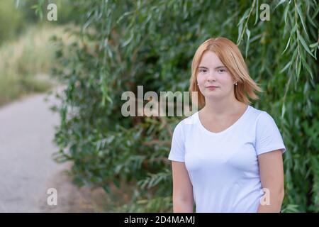 Ritratto di una giovane donna bionda felice in abiti bianchi. Passeggiata nel parco in estate, sfondo sfocato. Foto Stock