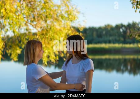 Due fidanzate si incontrano nel parco vicino al fiume. La bionda e la brunetta sono felici di vedersi. Fuoco selettivo, natura autunnale. Foto Stock