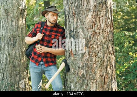 Elegante giovane uomo che posa come lumberjack. Raccolta di legname. Deforestazione. Legna da ardere come fonte di energia rinnovabile. Il Lumberjack che lavora in una foresta. Foto Stock