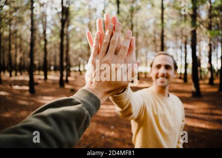 Giovani fratelli caucasici che danno un alto cinque e sorridendo mentre si trova in piedi in una foresta verde. Foto Stock