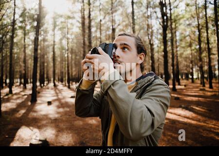 Giovane fotografo maschile nei boschi scattando foto con il suo videocamera Foto Stock