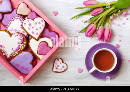 Biscotti al pan di zenzero, tè e un bouquet di tulipani. Composizione festosa con biscotti fatti in casa a forma di cuore e tulipani. Foto Stock