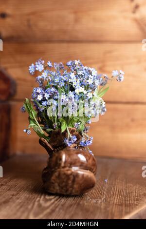 Bouquet non dimenticate di fiori in un vaso di ceramica su uno sfondo di legno. Foto Stock