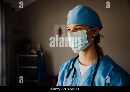 Primo piano di giovane infermiera caucasica femminile in scrub con maschera medica Foto Stock