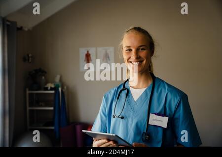 Primo piano ritratto di giovane dottoressa con scrub con tavoletta, sorridente e felice Foto Stock