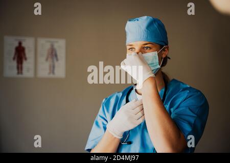 Donna caucasica o chirurgo in scrub preparazione per chirurgia, guanti medici e maschera Foto Stock