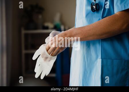 Primo piano di medico femminile in scrub mettendo guanti chirurgo sulle mani Foto Stock