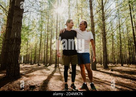 Il padre e il figlio caucasici abbracciano dopo una corsa insieme dentro i boschi Foto Stock