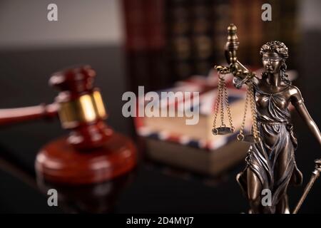 Tema della legge. Camera di giudizio. La gavella del giudice, la statua di Themis e la collezione di libri legali sulla scrivania marrone e sullo sfondo marrone. Foto Stock