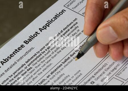 Mano tenendo una penna e compilando un modulo di candidatura per l'iscrizione al voto degli Assentee dello Stato di New York. Fuoco selettivo sul modulo. Foto Stock