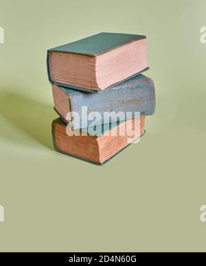 Una pila di tre vecchi libri si trova su uno sfondo verde chiaro. Formato verticale Foto Stock