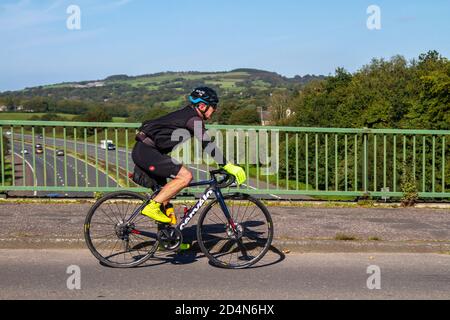 Cavalcare il ciclista maschile Cervalo sport in fibra di carbonio bici da strada sulla strada di campagna che attraversa il ponte autostradale nel Lancashire rurale, Regno Unito Foto Stock