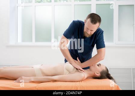 Terapeuta manuale osteopatica maschile adulta che esegue la manipolazione fisica e il massaggio petto di paziente femminile in clinica moderna Foto Stock