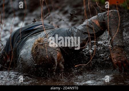 Corridore di corsa del fango, uomo che corre nel fango. Guide durante le gare di ostacoli estremi. Concetto di vita attiva e sport Foto Stock