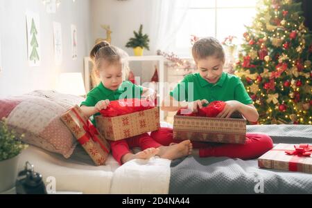 Buon Natale e buone feste! Allegro cute bambine apertura regali sul letto. I bambini indossano pigiami che si divertono vicino all'albero al mattino. Foto Stock