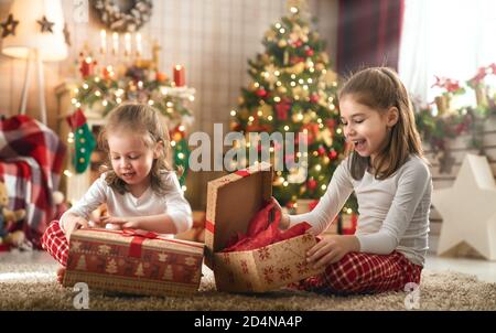 Buon Natale e buone feste! Allegro cute bambine apertura regali. I bambini indossano pigiami che si divertono vicino all'albero al mattino. Amore fami Foto Stock