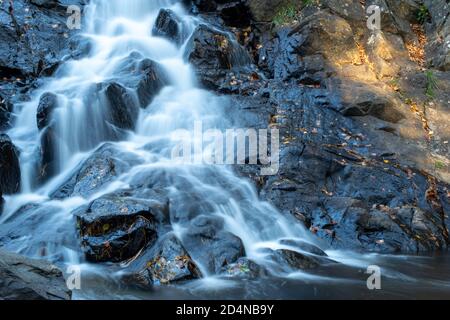 Cascata eterea a lunga esposizione su rocce nere in luce crepata. Foto Stock