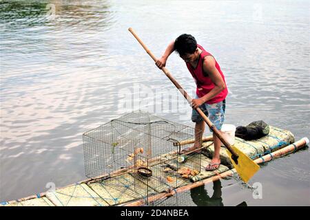 Un uomo cattura il pesce in un lago utilizzando un makeshift barca fatta di schiuma di plastica e pali di bambù Foto Stock