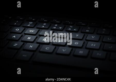 Primo piano della tastiera QWERTY nera del notebook con la luce che cade sui tasti. Foto Stock