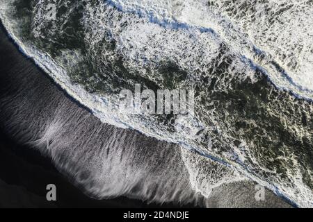 Pile astratte di onde sulla spiaggia di sabbia nera, vista dall'alto verso il basso. Foto Stock
