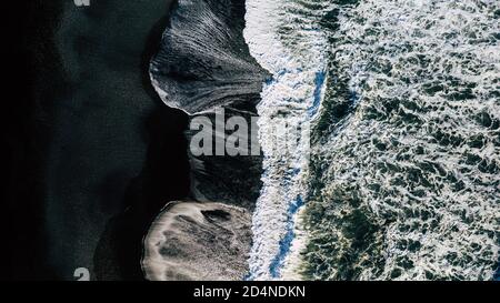Pile astratte di onde sulla spiaggia di sabbia nera, vista dall'alto verso il basso. Foto Stock