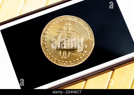 Moneta d'oro Bitcoin sullo schermo dello smartphone, primo piano, vista dall'alto. Moneta d'oro sul display di un telefono cellulare, visto dall'alto, app criptovaluta trading Foto Stock