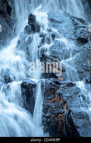 La cascata a lunga esposizione si schianta su rocce nere frastagliate. Foto Stock