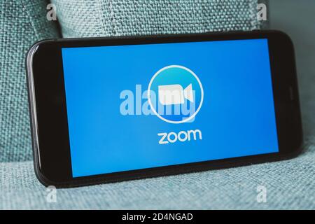 Telefono con una mano che mostra l'app Zoom Cloud Meetings. Lavoro e riunioni da casa con uno smartphone. Foto Stock