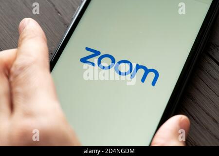 Telefono con una mano che mostra l'app Zoom Cloud Meetings. Lavoro e riunioni da casa con uno smartphone. Foto Stock