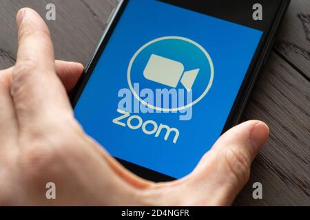 Telefono con una mano che mostra l'app Zoom Cloud Meetings. Lavoro e riunioni da casa con uno smartphone. Foto Stock